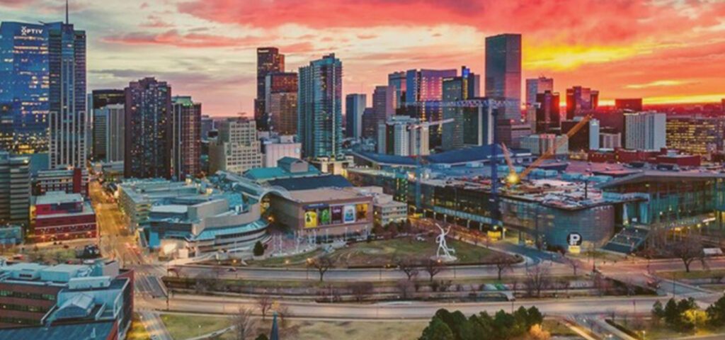Denver skyline at sunset with illuminated skyscrapers under a vibrant orange sky - Lederhosen For Sale