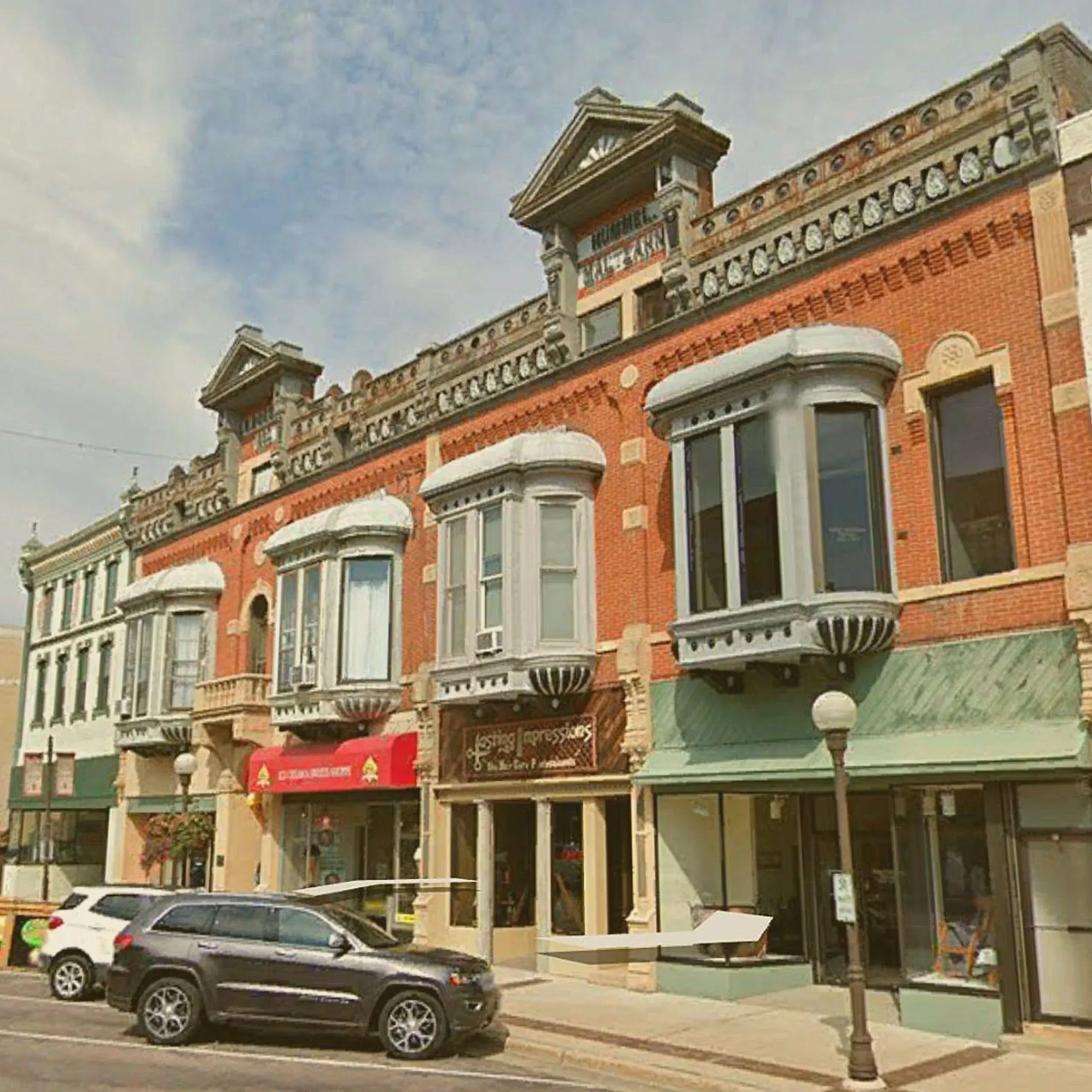 A row of historic brick storefronts on a city street, including the Boesch, Hummel, and Maltzahn Block building in New Ulm. - Lederhosen For Sale