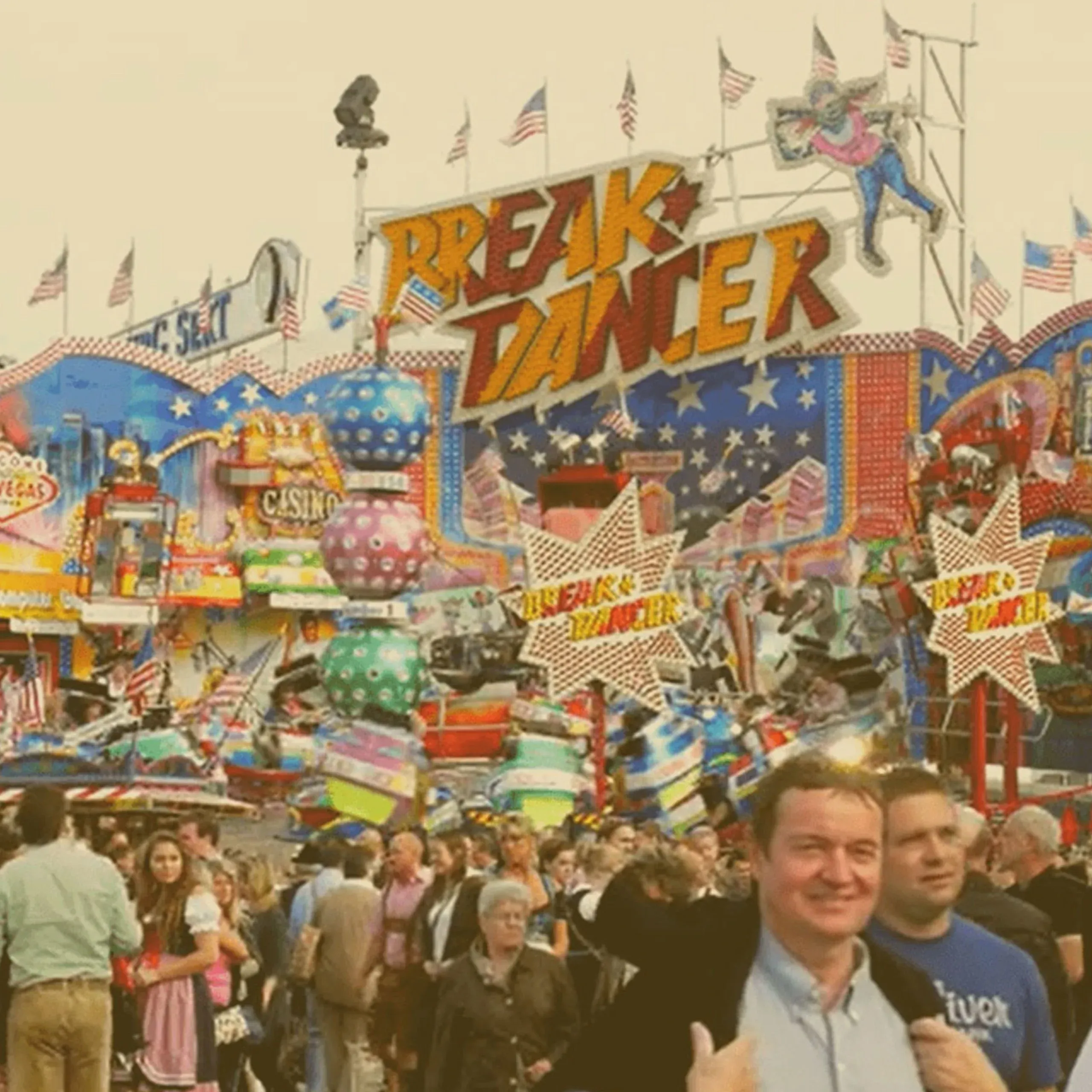 A crowded amusement park scene at an Oktoberfest event in Ohio, featuring a large "Break Dancer" spinning ride with colorful signs and flags. - Lederhosen For Sale