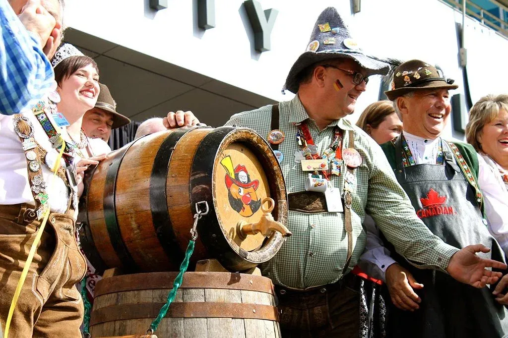 People gathered around a traditional wooden beer barrel at a festive Oktoberfest celebration. - Lederhosen For Sale