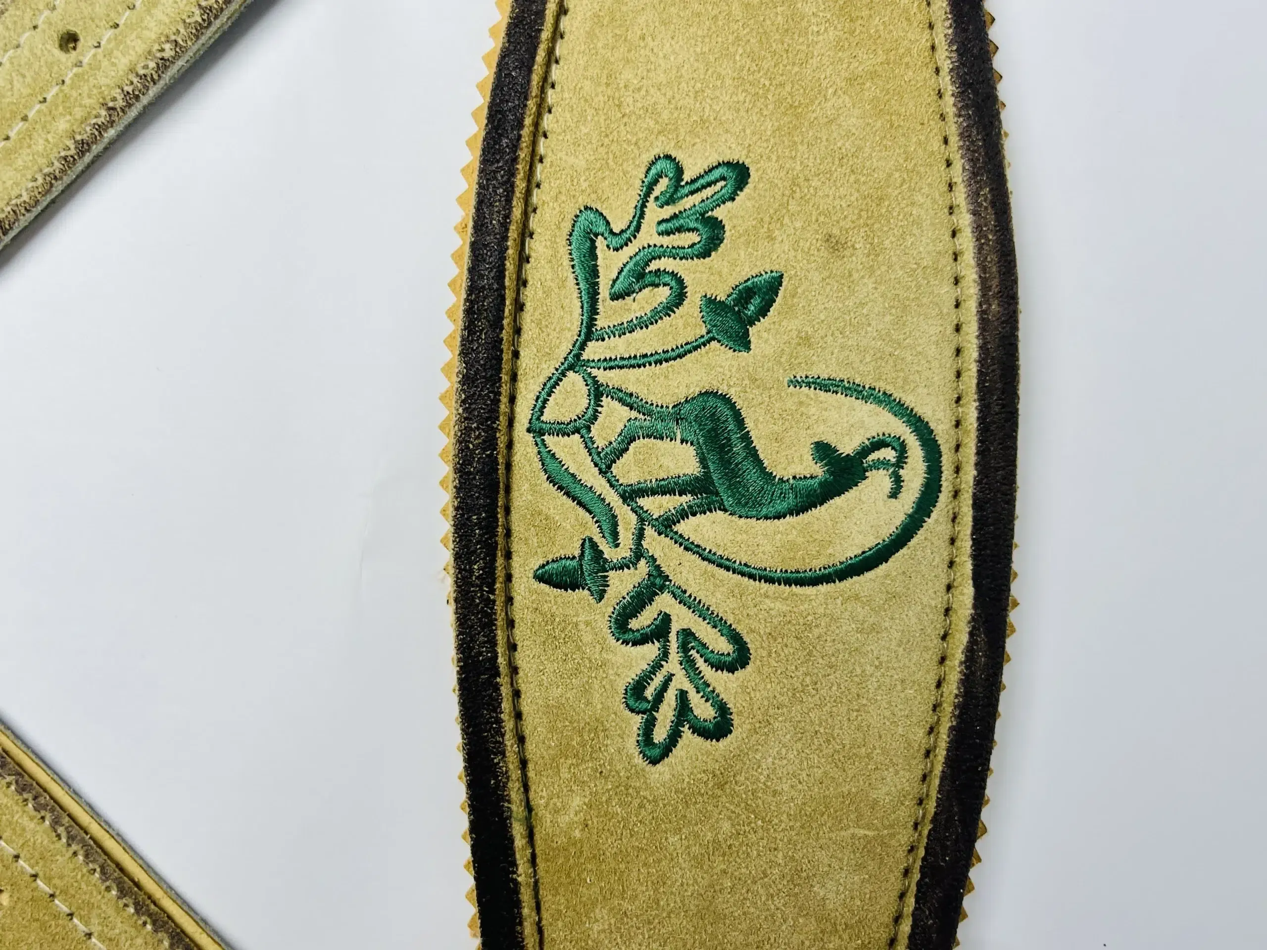 Close-up of green oak leaf and acorn embroidery on a light gold Lederhosen suede suspender strap. - Lederhosen For Sale