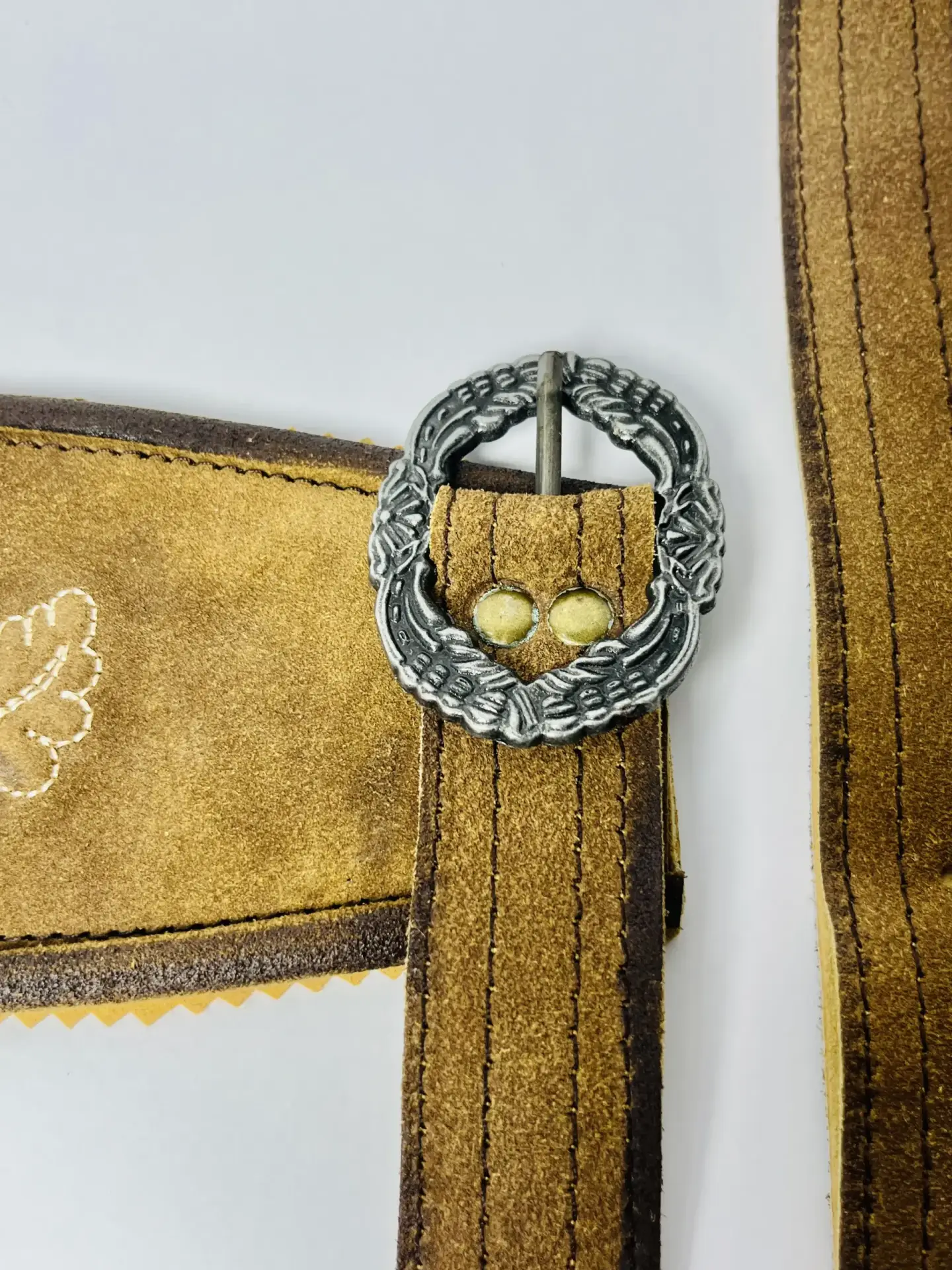 Close-up of a vintage brown Lederhosen suede suspender strap fastened with a detailed antique silver oval buckle. - Lederhosen For Sale
