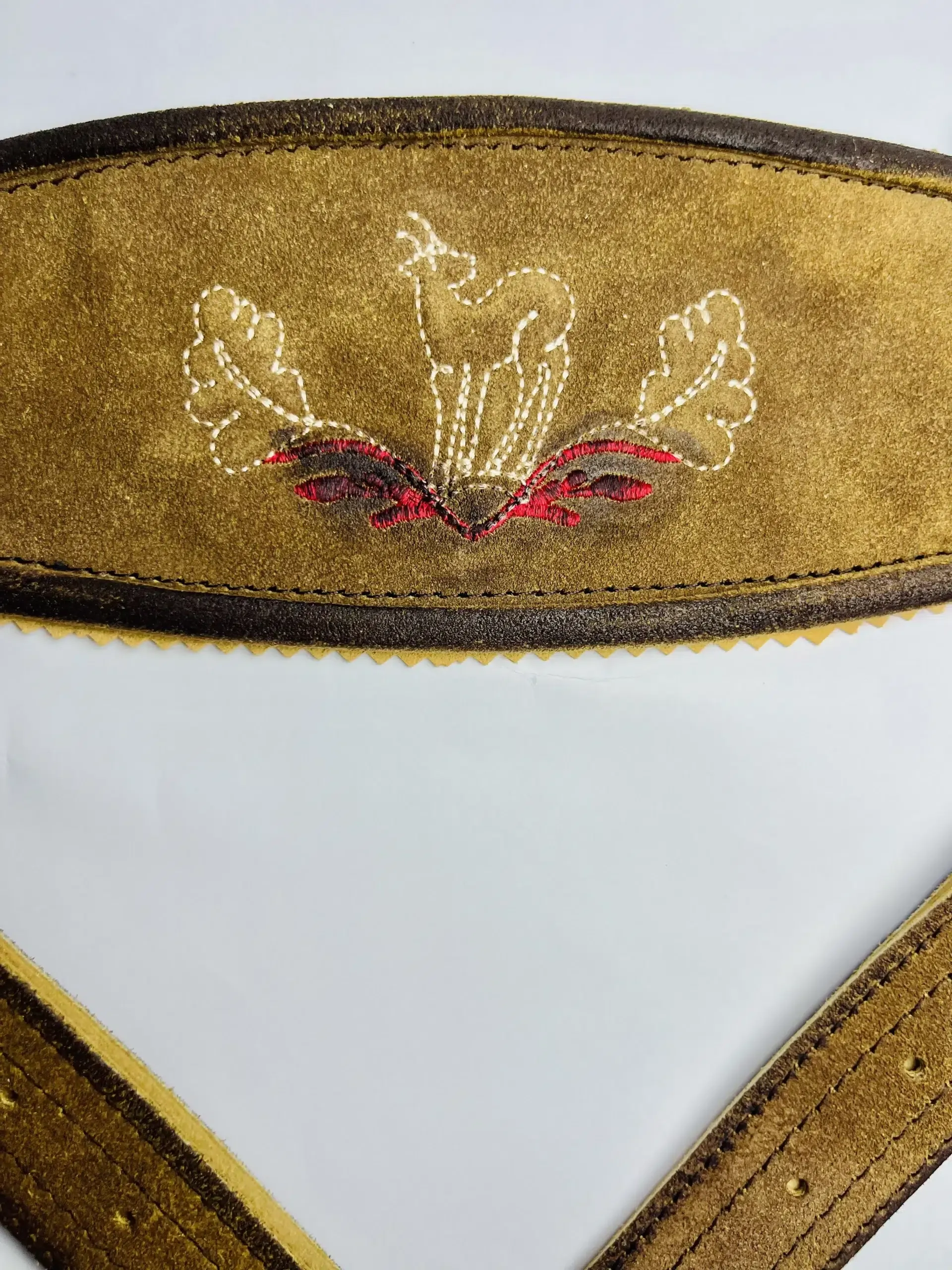 Close-up of white stag and oak leaf embroidery with subtle red accents on a vintage brown Lederhosen suspender cross-bridge. - Lederhosen For Sale